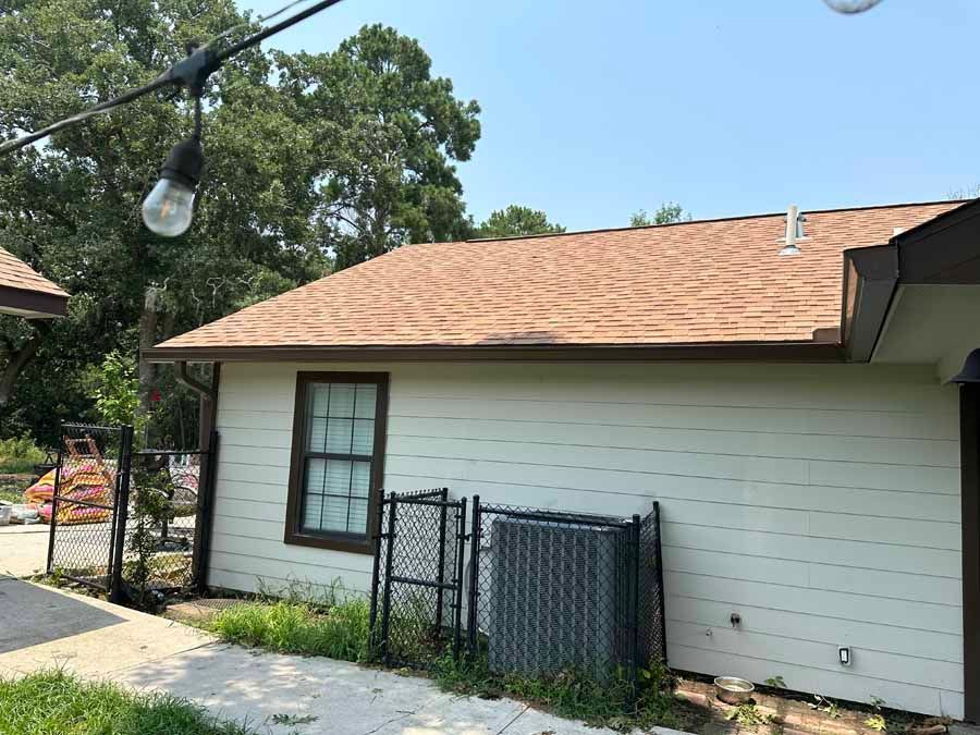 A white house with a brown roof and a fence in front of it.