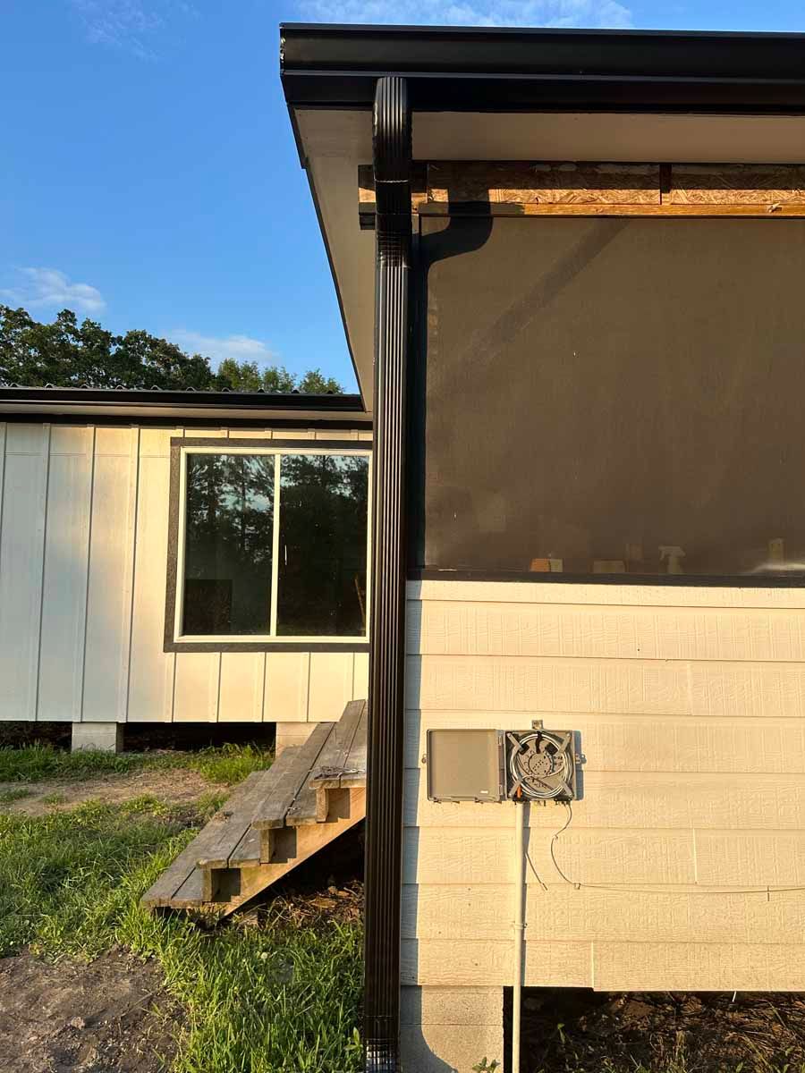 A white house with a black gutter on the side of it.