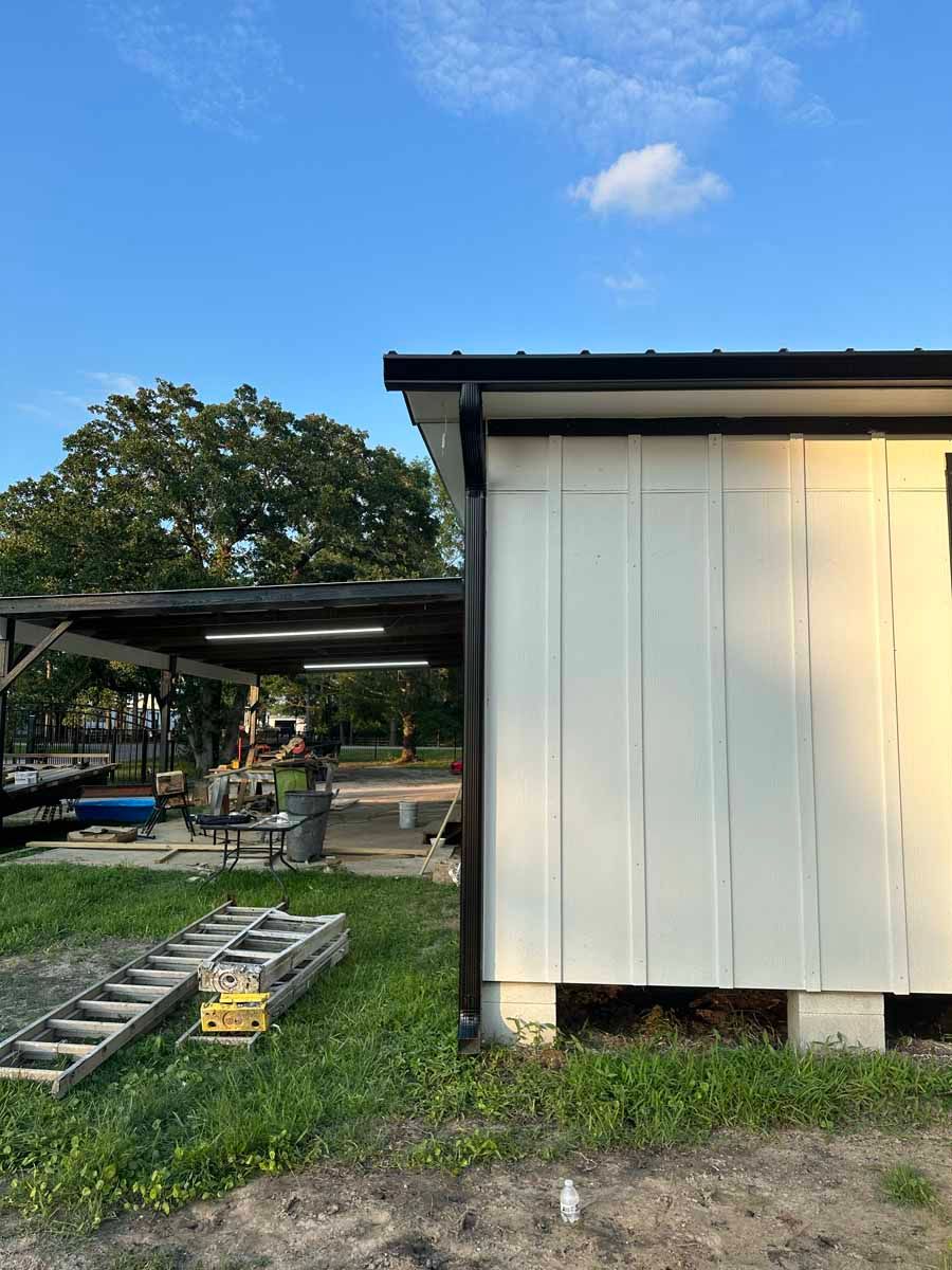 A white shed is sitting in the middle of a grassy field.