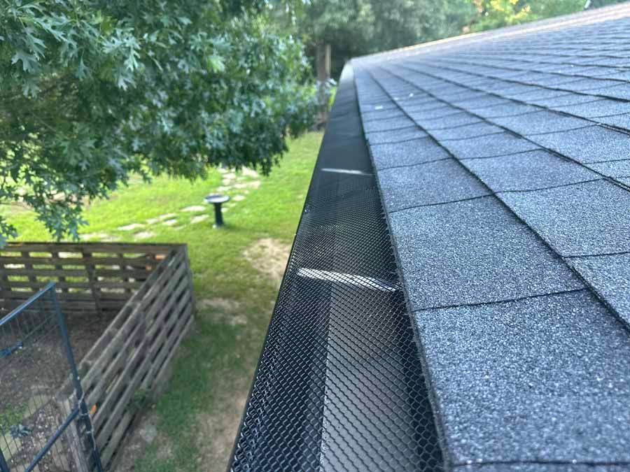 A close up of a gutter on a roof with a fence in the background.