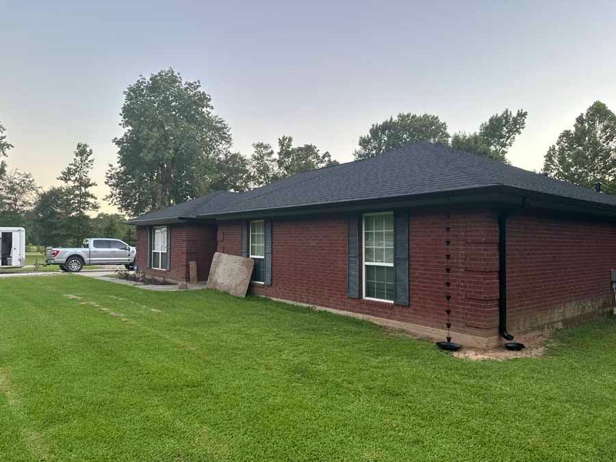 A red brick house with a black roof is sitting on top of a lush green field.