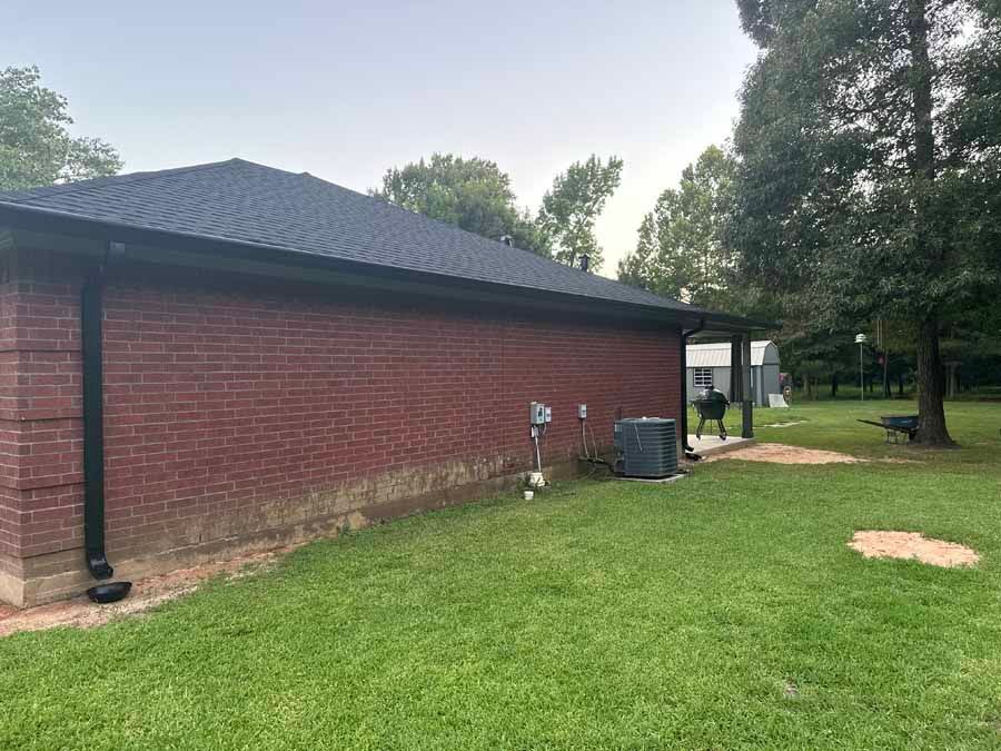A brick house with a black roof and a large lawn in front of it.