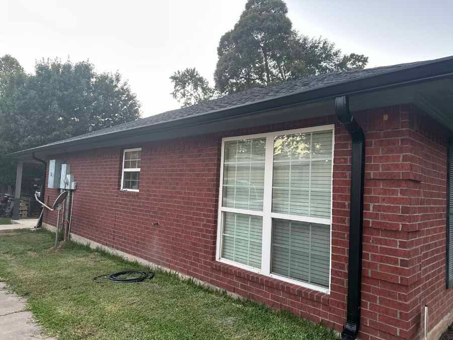 A red brick house with a black gutter and white windows.
