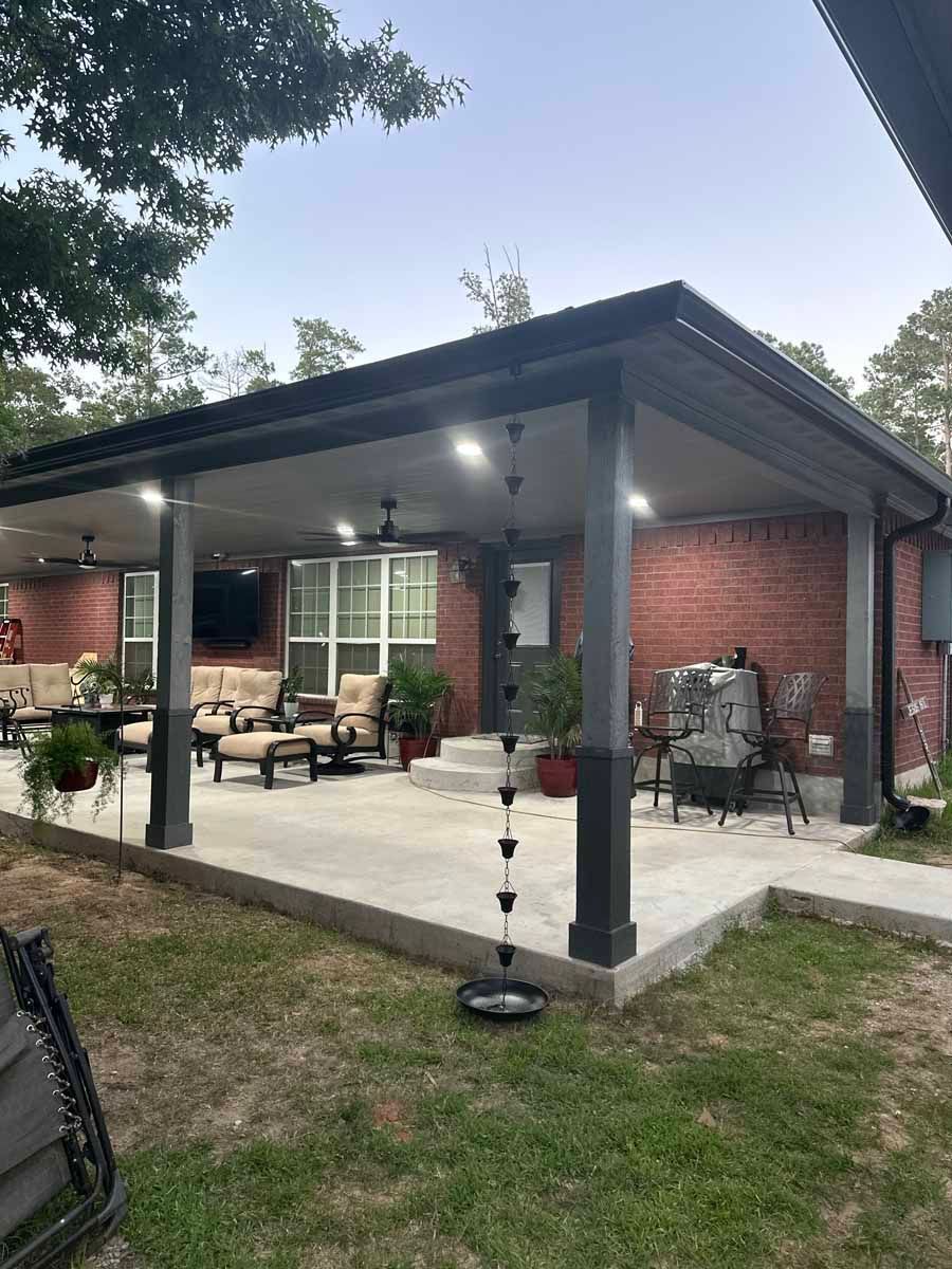 A large covered patio with a brick house in the background.