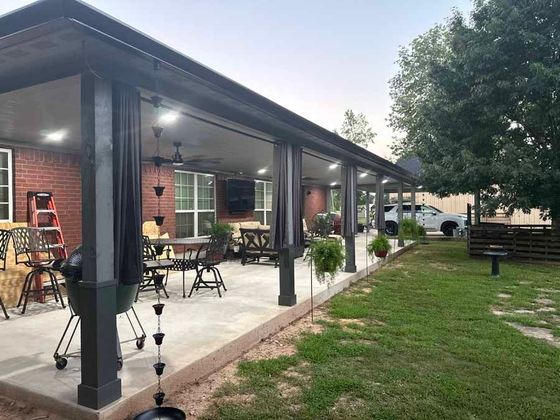 A large covered patio with tables and chairs and a grill.