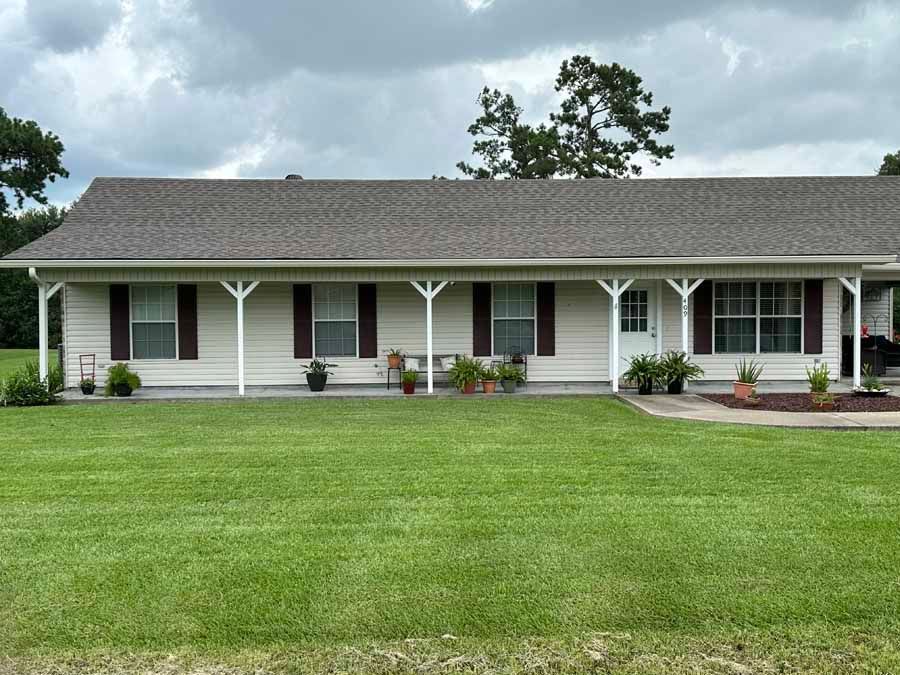 A white house with brown shutters and a large lawn in front of it.