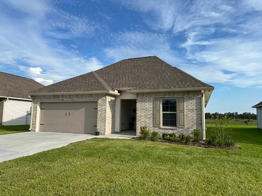 A brick house with a garage and a large lawn in front of it.