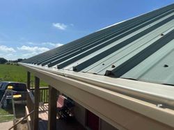 A green metal roof with a white gutter on a porch.