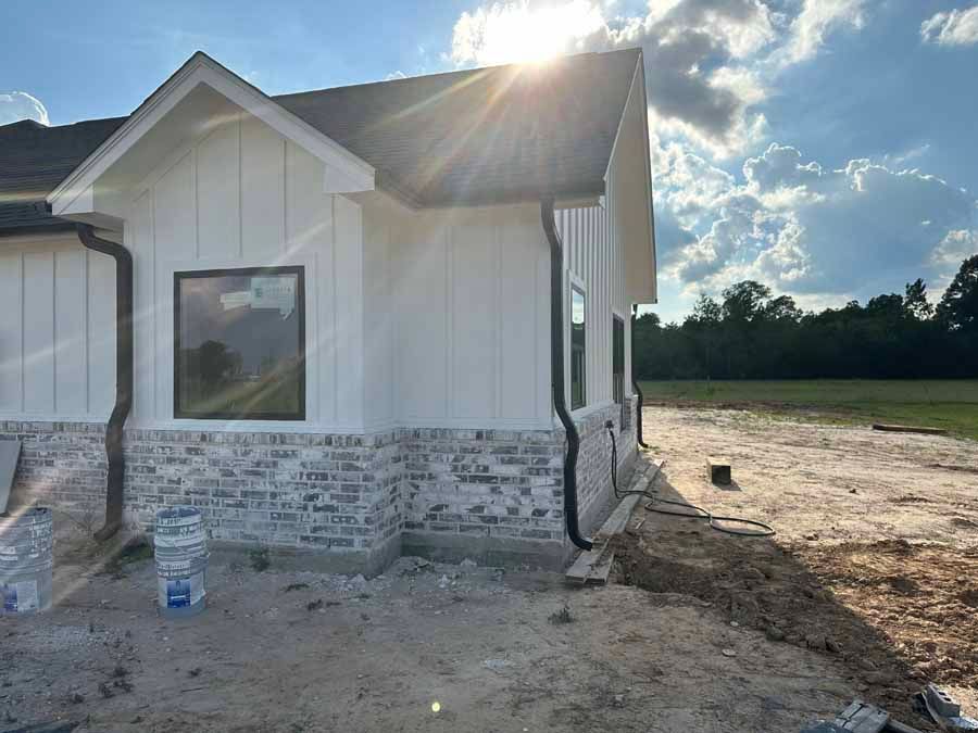 A white house with a black roof is being built in a dirt field.