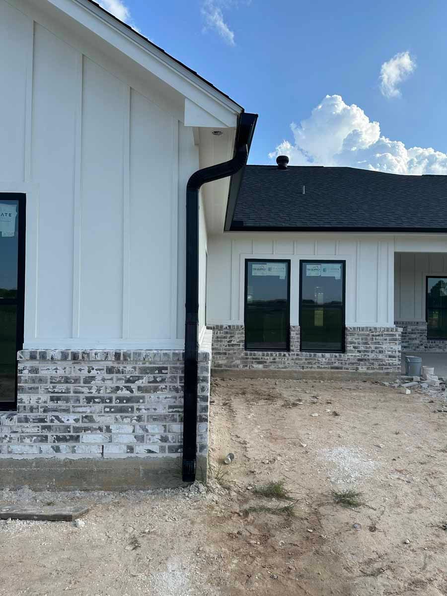 A white house with a black gutter on the side of it.