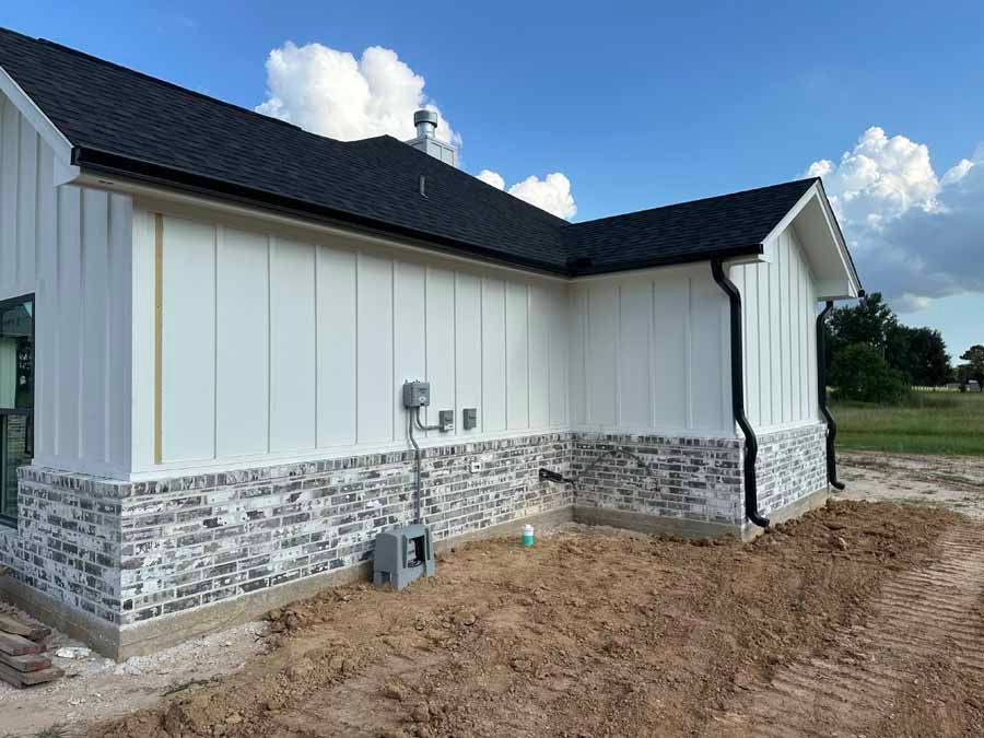 A white house with a black roof is sitting on top of a dirt field.