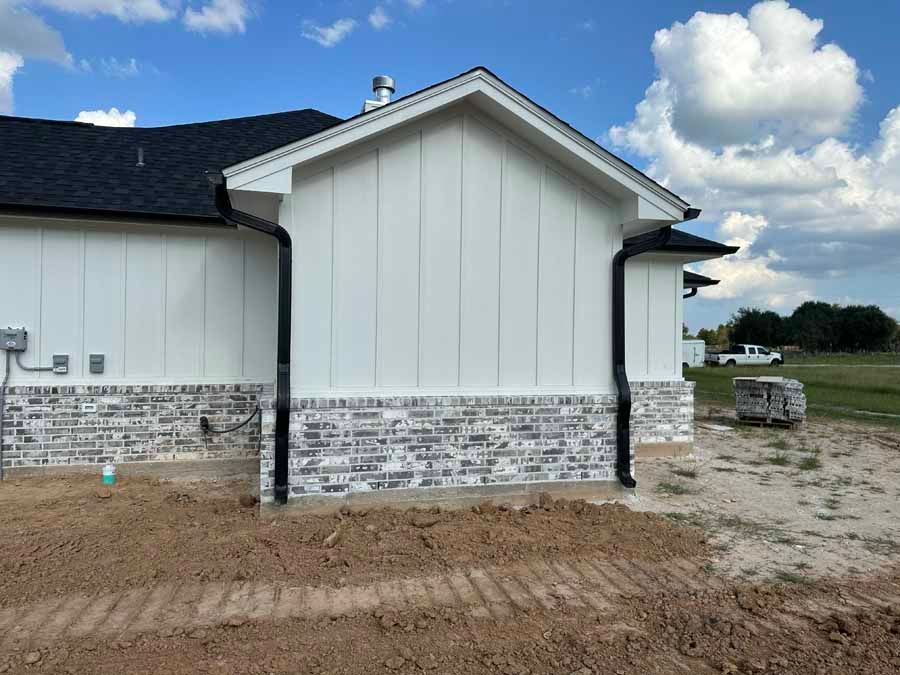 A white house with a black roof is sitting on top of a dirt field.