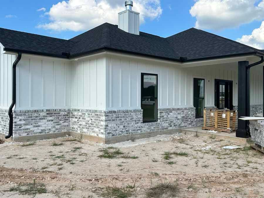 A white house with a black roof is sitting on top of a dirt field.