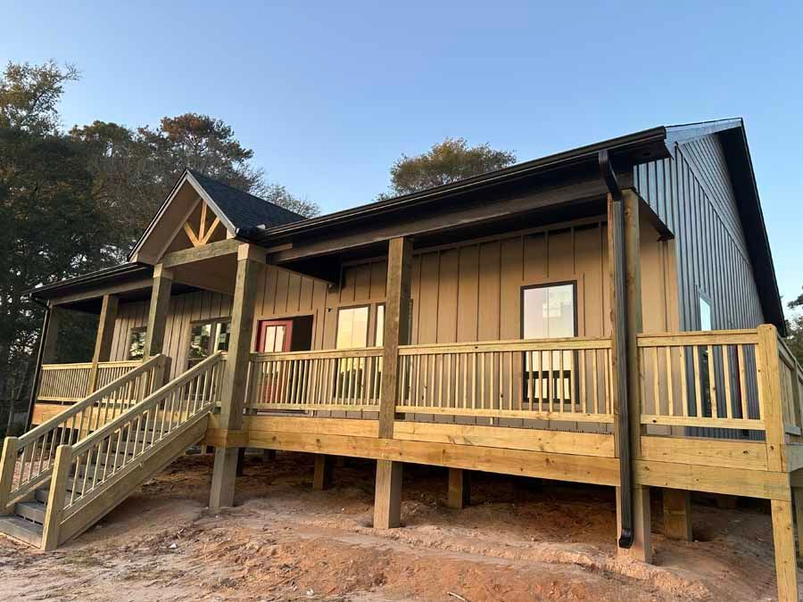 A house with a wooden deck and stairs is sitting on top of a dirt hill.