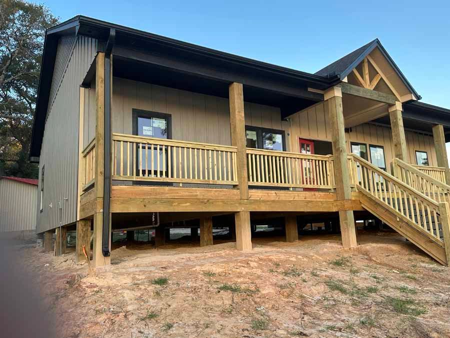 A house with a wooden deck and stairs is sitting on top of a dirt hill.