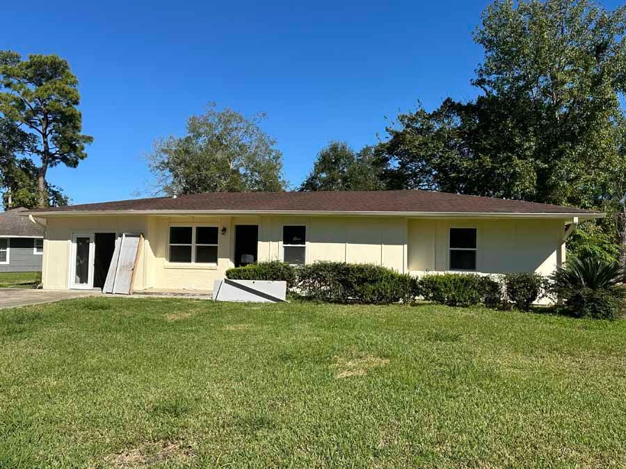 A white house with a brown roof is sitting on top of a lush green field.