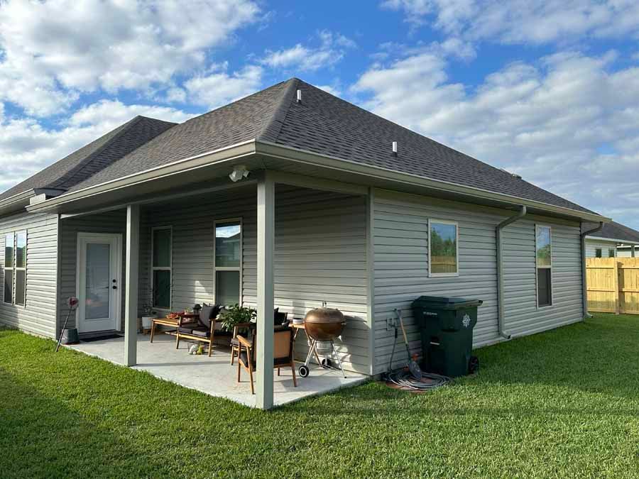 The back of a house with a covered patio and a trash can.