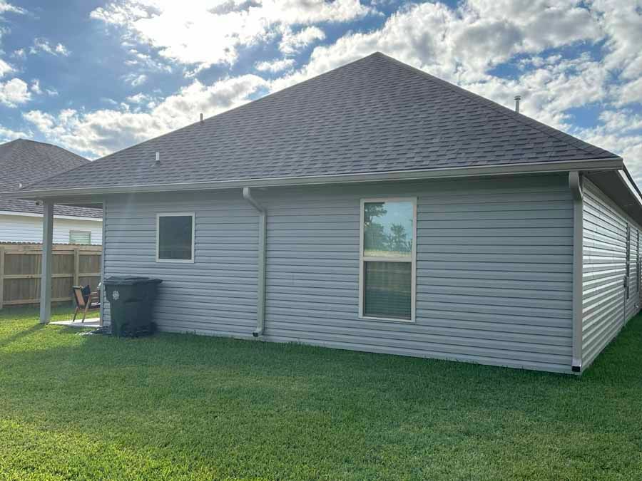 The back of a house with a lot of windows and a trash can in the backyard.
