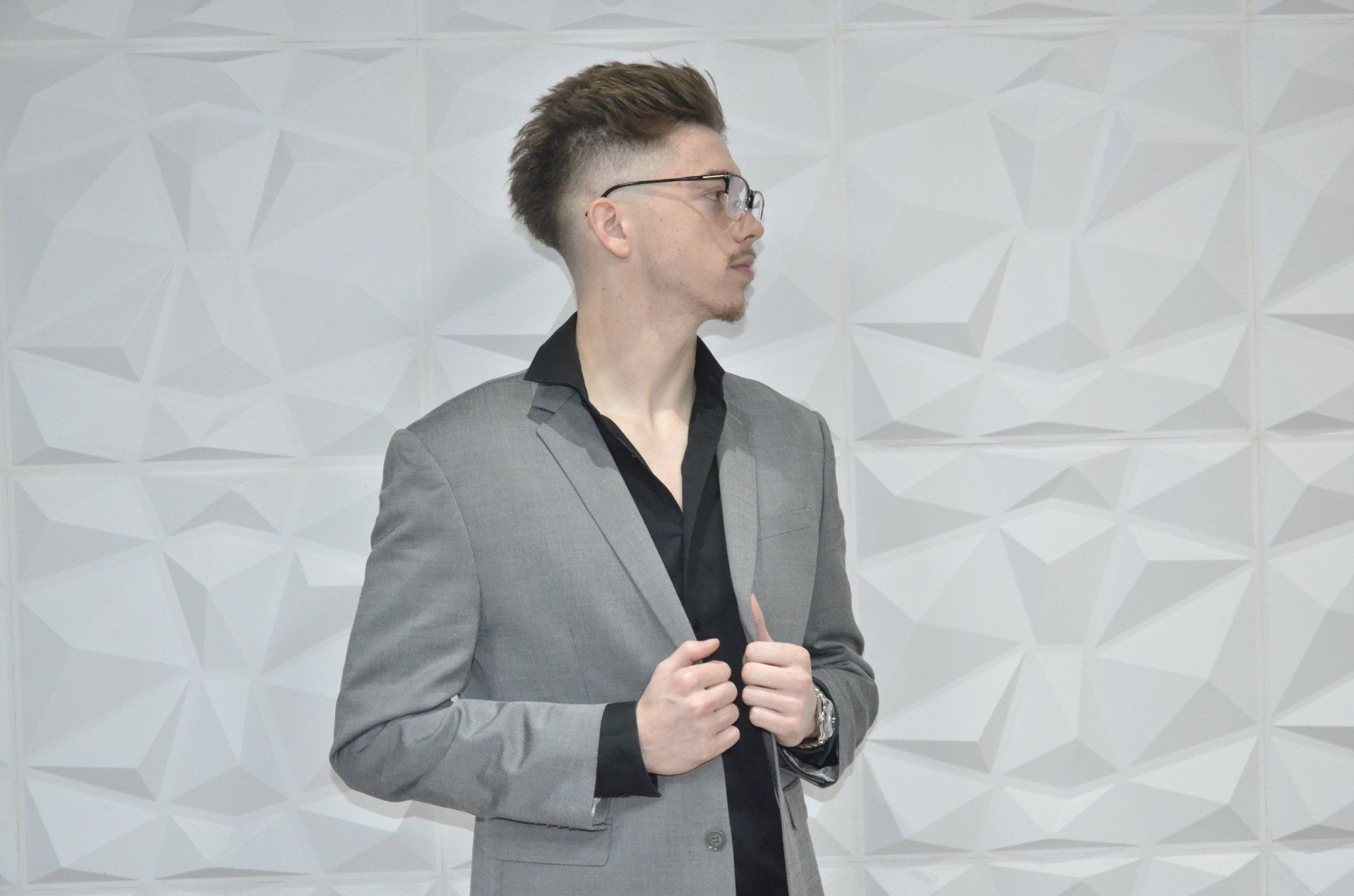 a man in a suit and glasses is standing in front of a white wall .