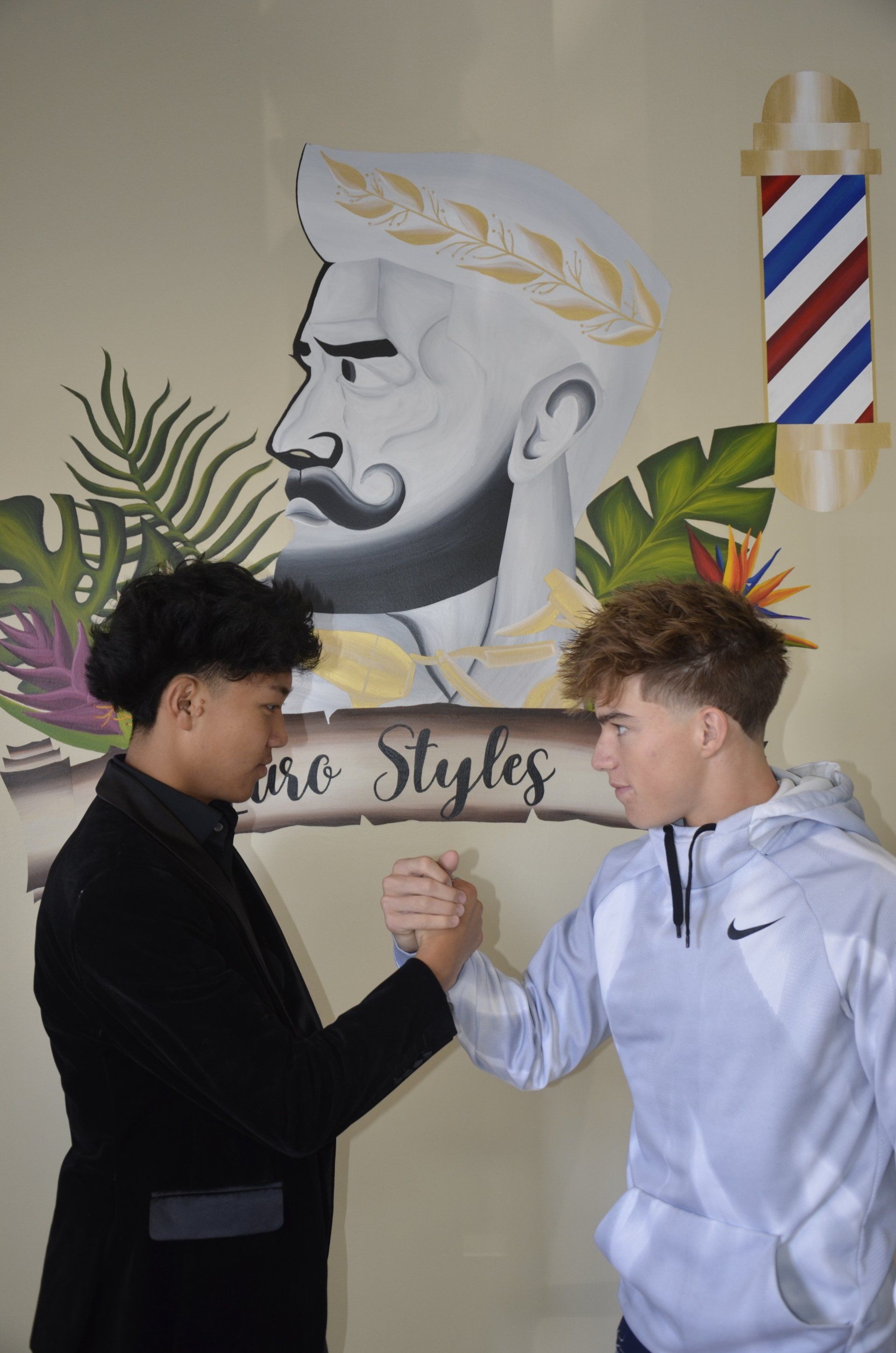 two young men are shaking hands in front of a barber pole .