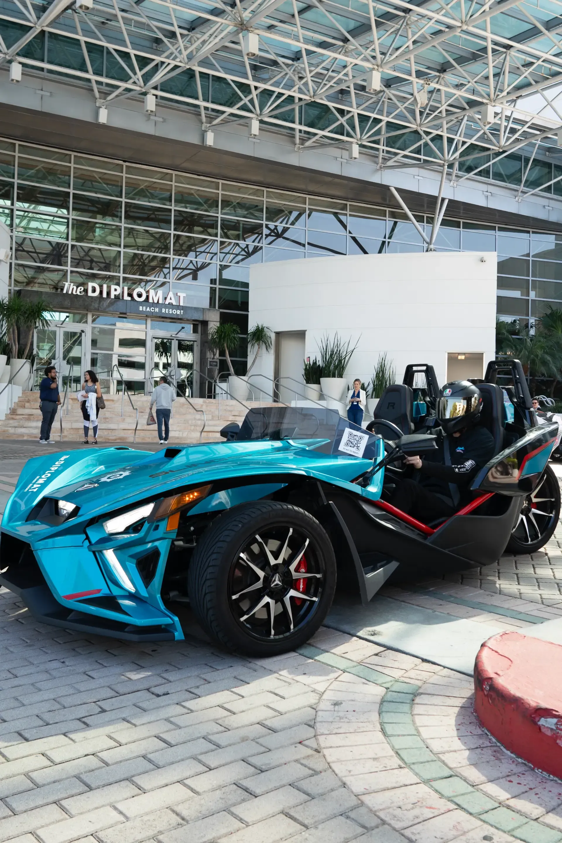 A blue slingshot is parked in front of a building.