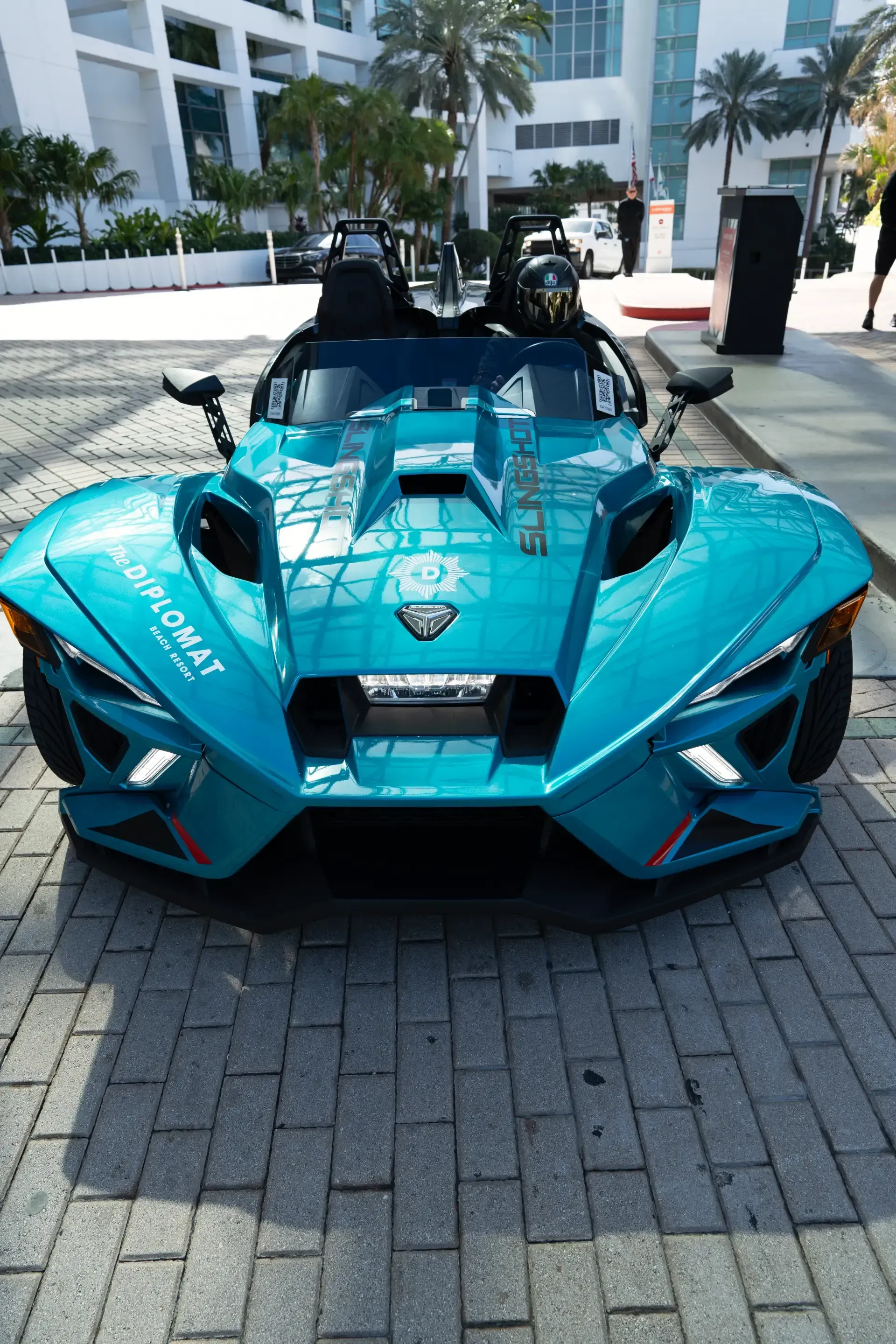 A blue slingshot is parked on a brick sidewalk in front of a building.