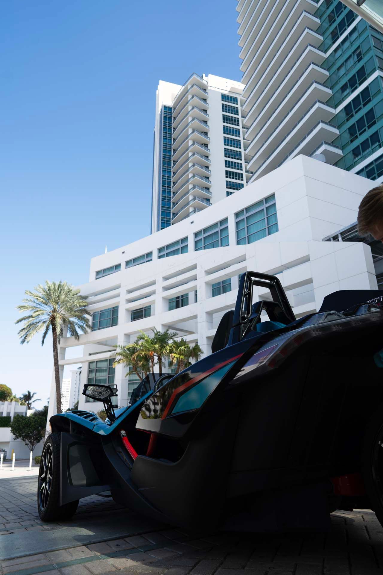 A slingshot is parked in front of a tall building.