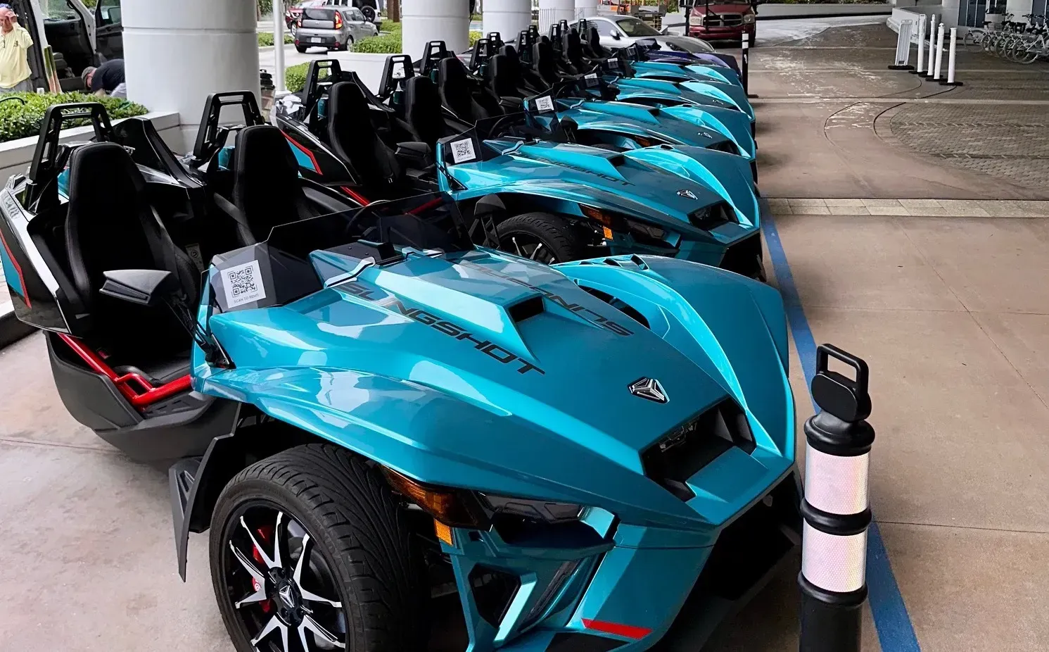 A row of blue slingshot motorcycles are parked in a parking lot.