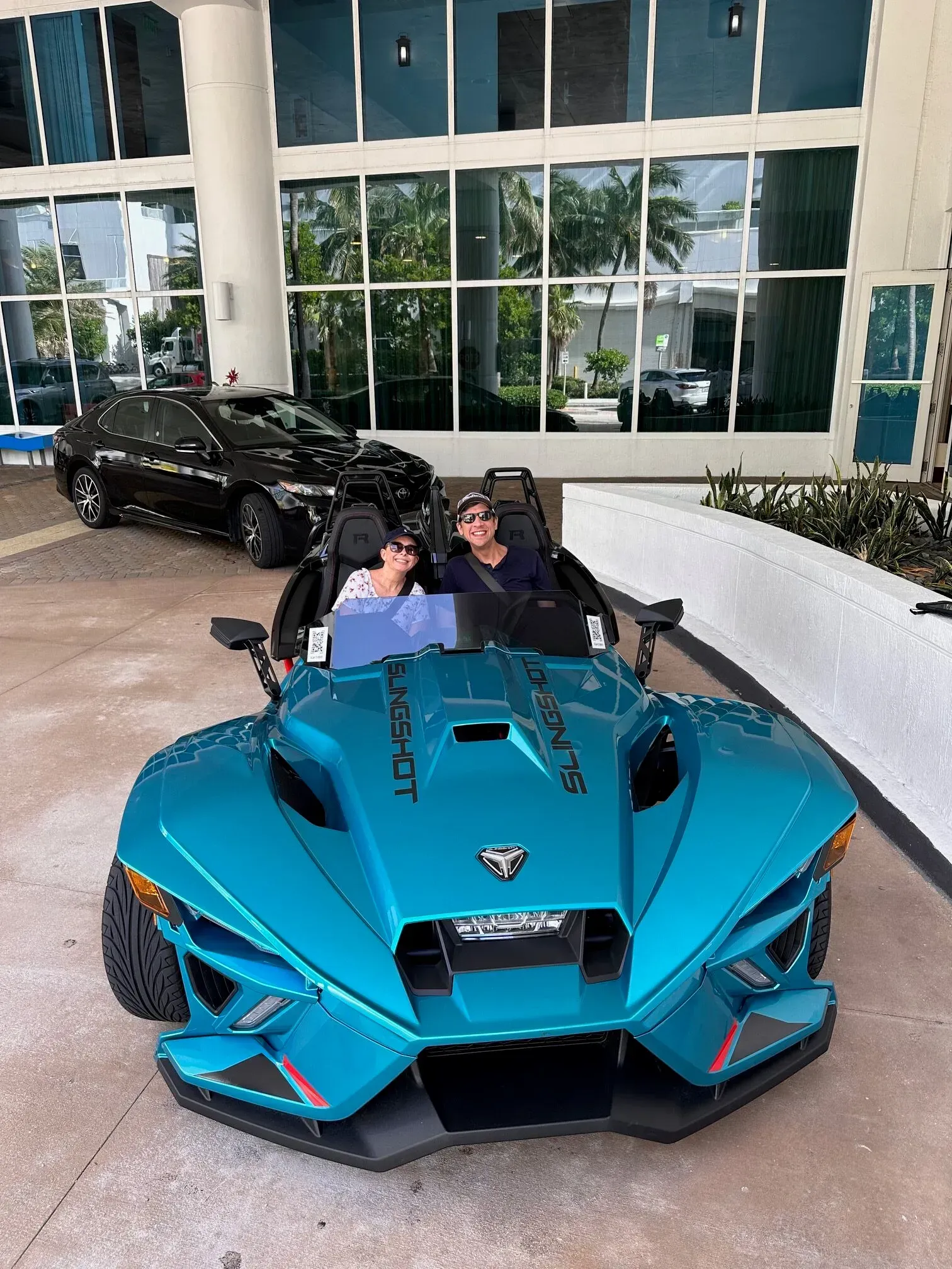 A couple is sitting in a blue slingshot in front of a building.