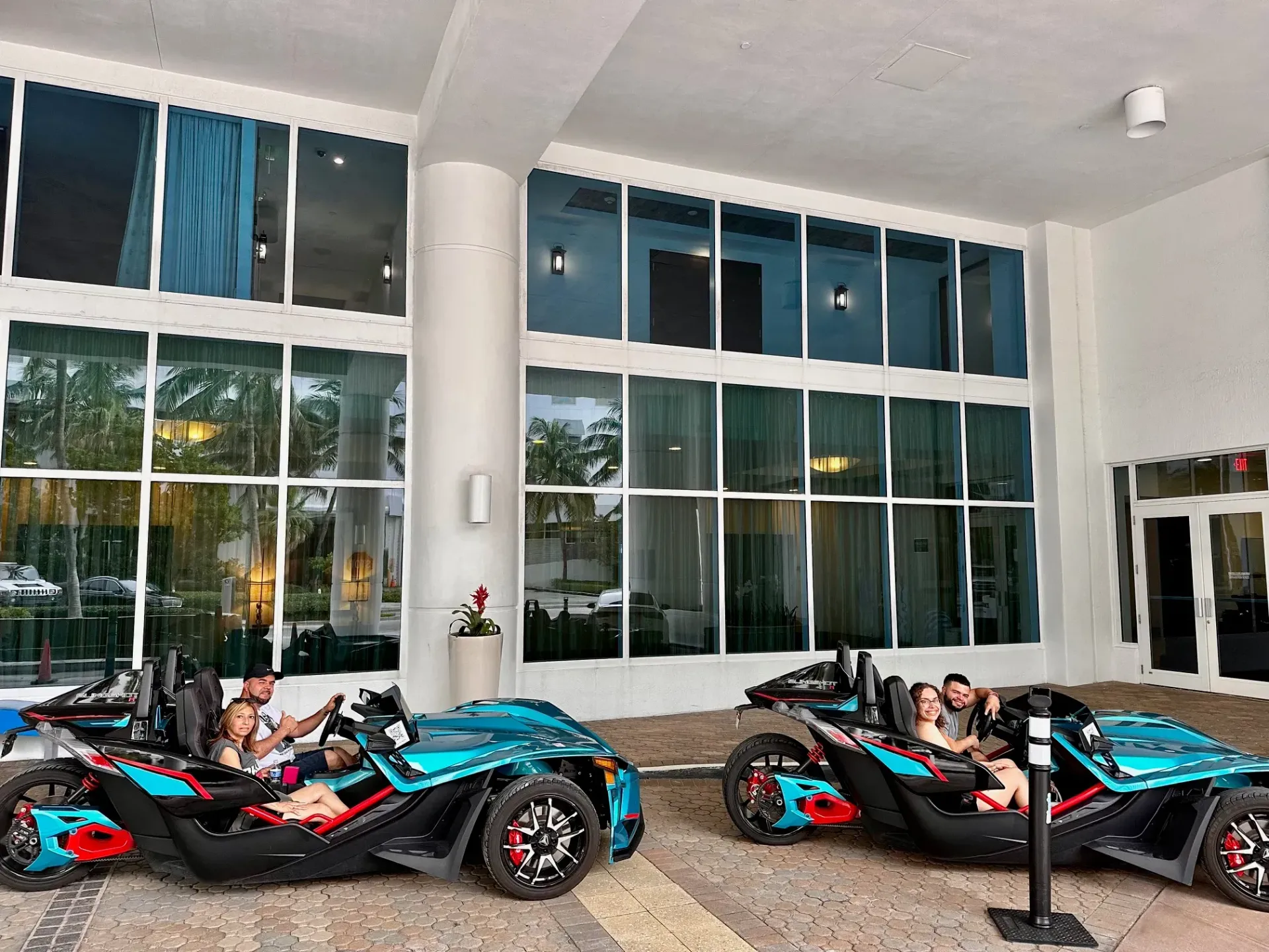 Two slingshot cars are parked in front of a building.