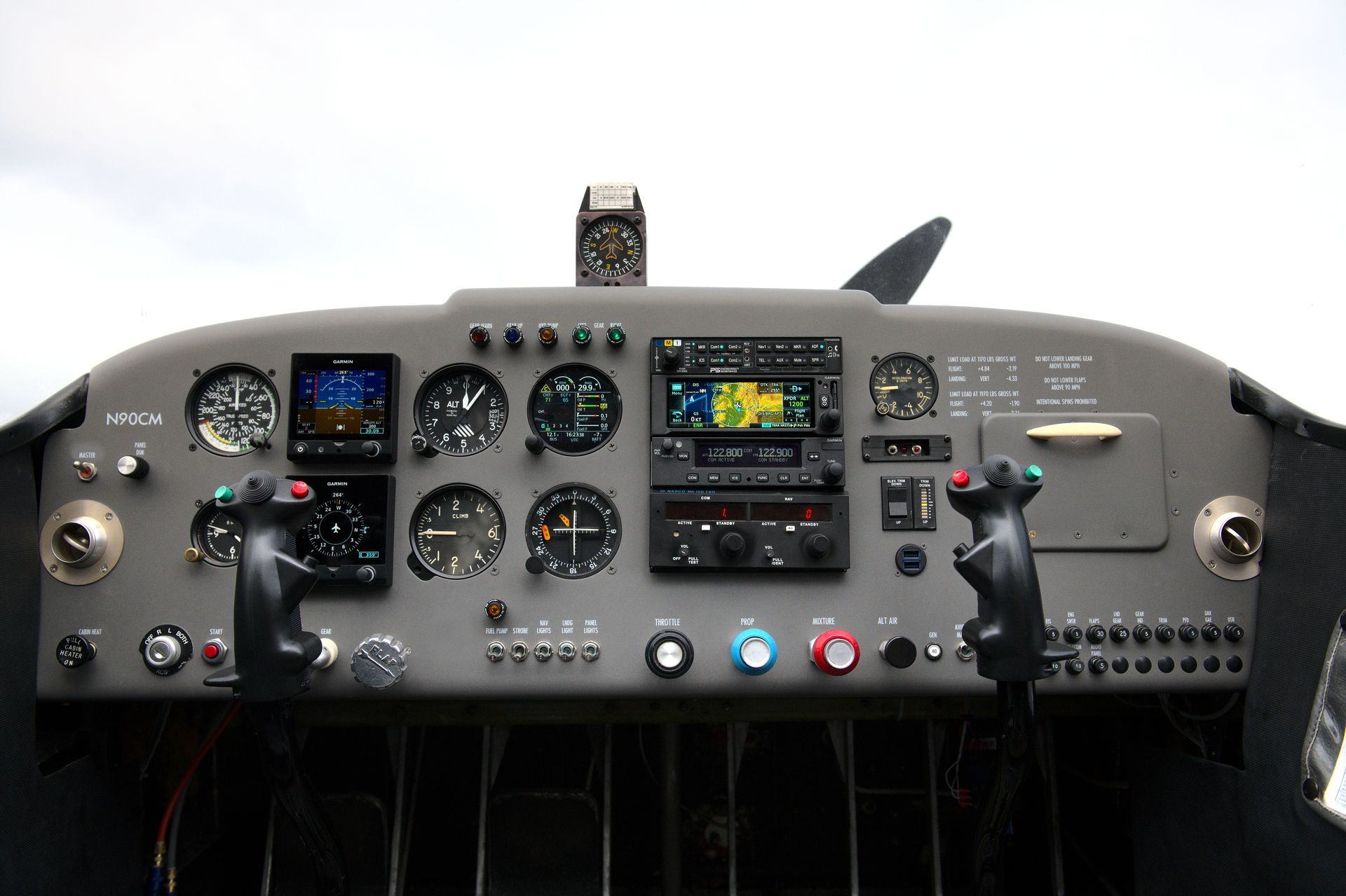 Aircraft cockpit with gray dashboard and various gauges, controls, and two control sticks.