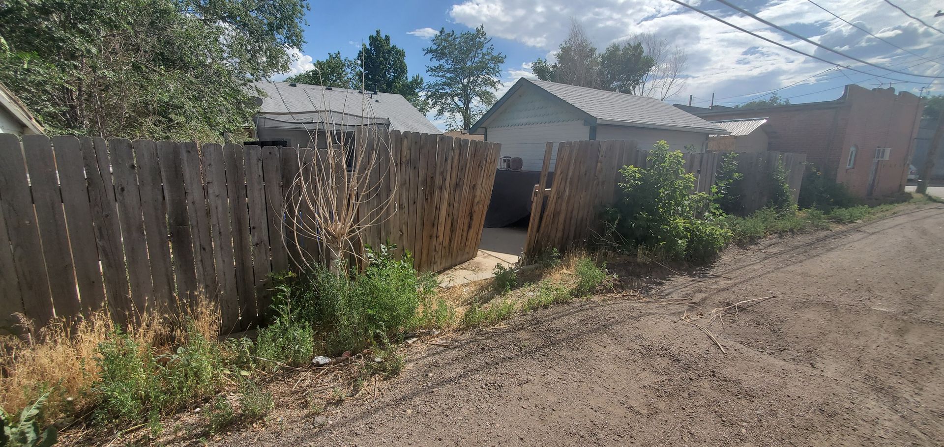 A wooden fence surrounds a dirt road next to a house.