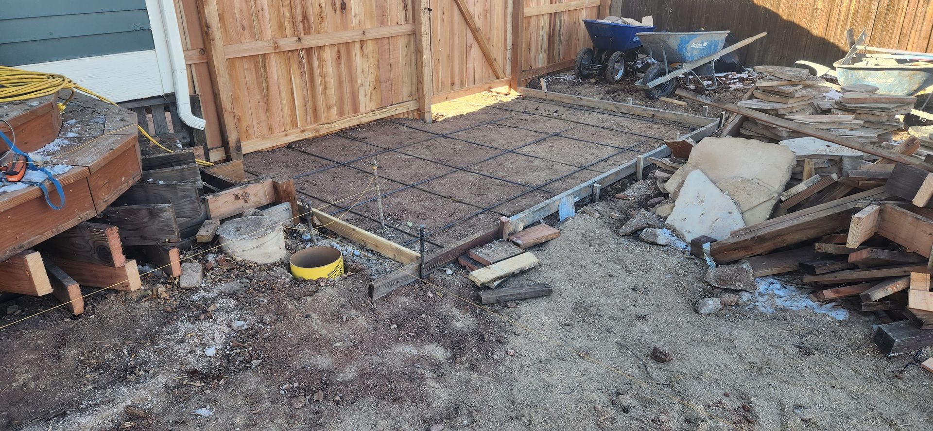 A pile of wood is sitting in the dirt in front of a wooden fence.