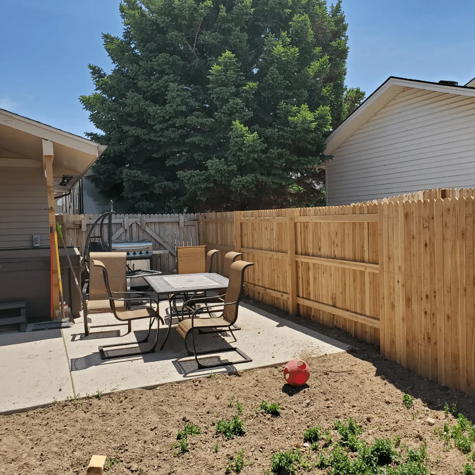 A wooden fence surrounds a patio with a table and chairs.