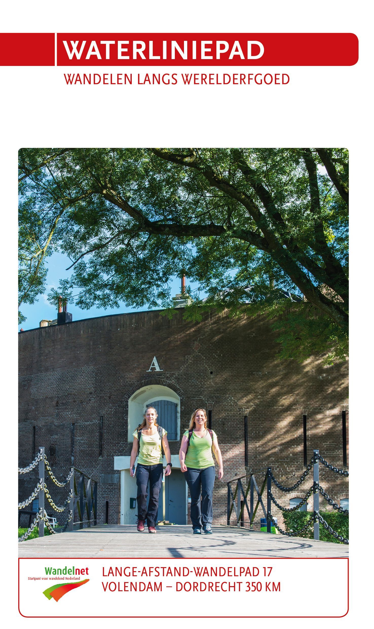 Twee vrouwen lopen over een brug bij een bakstenen gebouw, onder een boom. Titel: 