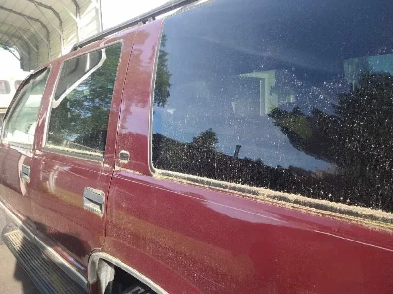 A red car with a black window is parked in front of a building.