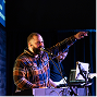 Singer in a plaid shirt performing at a microphone with a raised arm under blue stage lights