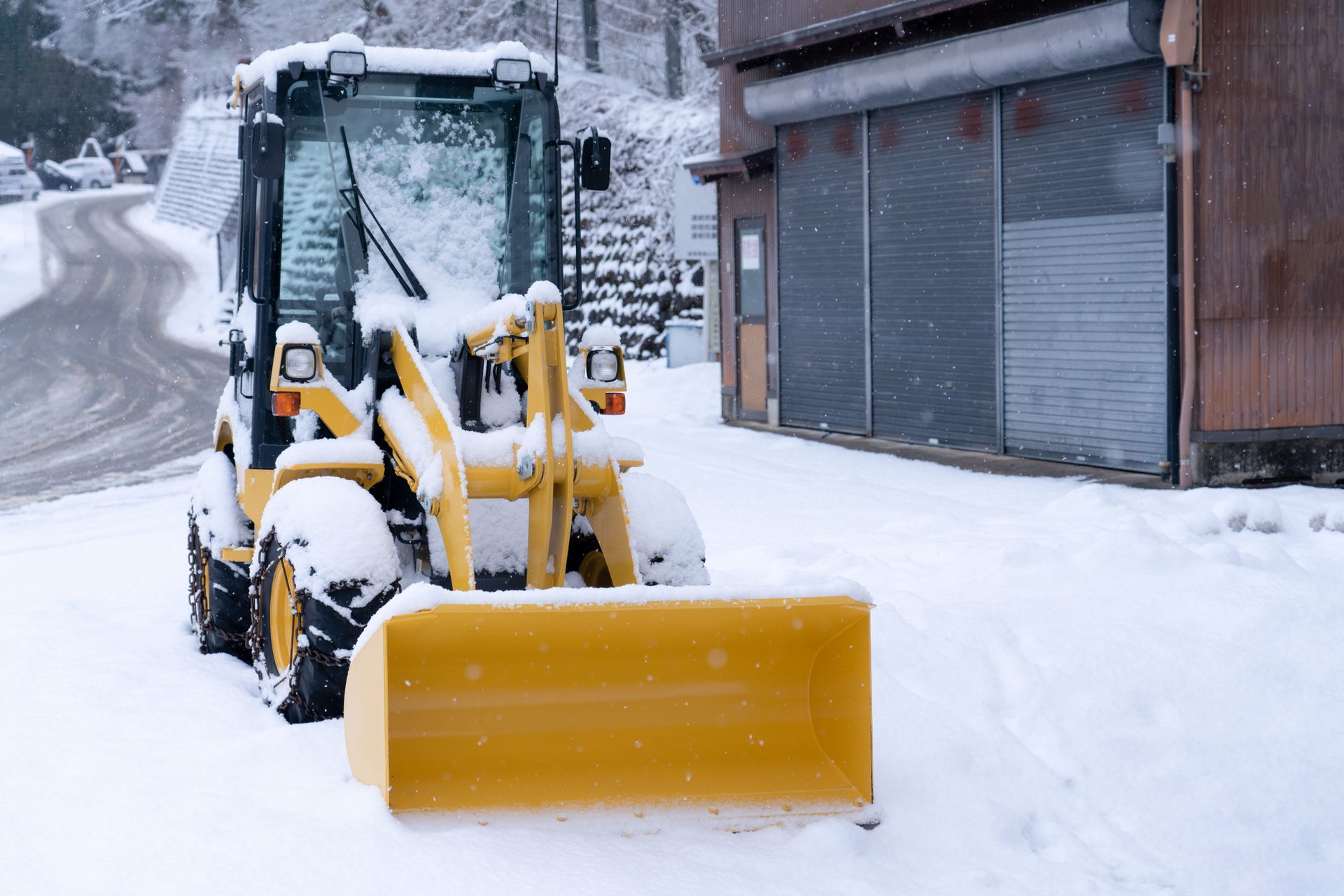Yellow snowplow parked on snow-covered street next to a building, winter scene.