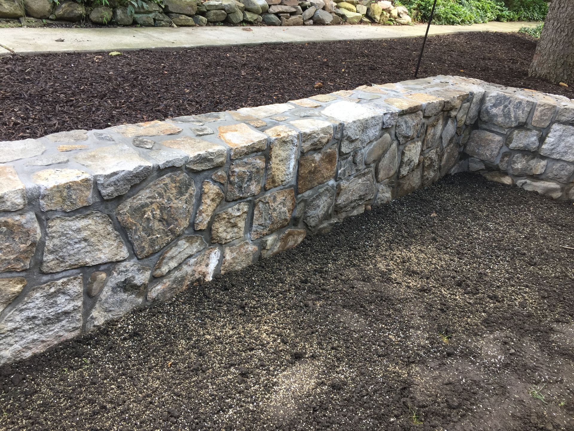Stone retaining wall with a bed of seeds and mulch in a garden.