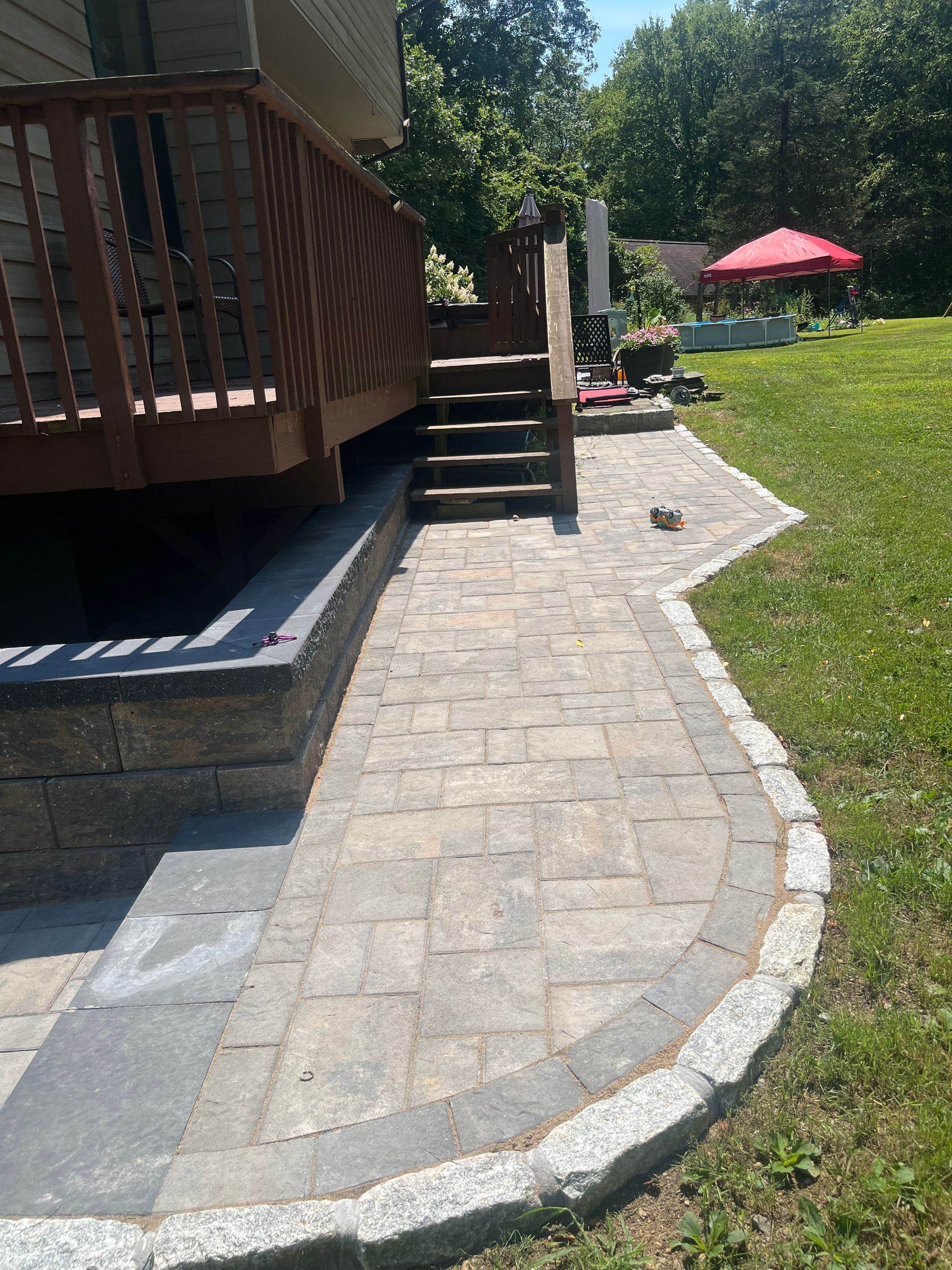 Brick pathway leading to deck stairs, bordered by granite and grass. Sunny day.