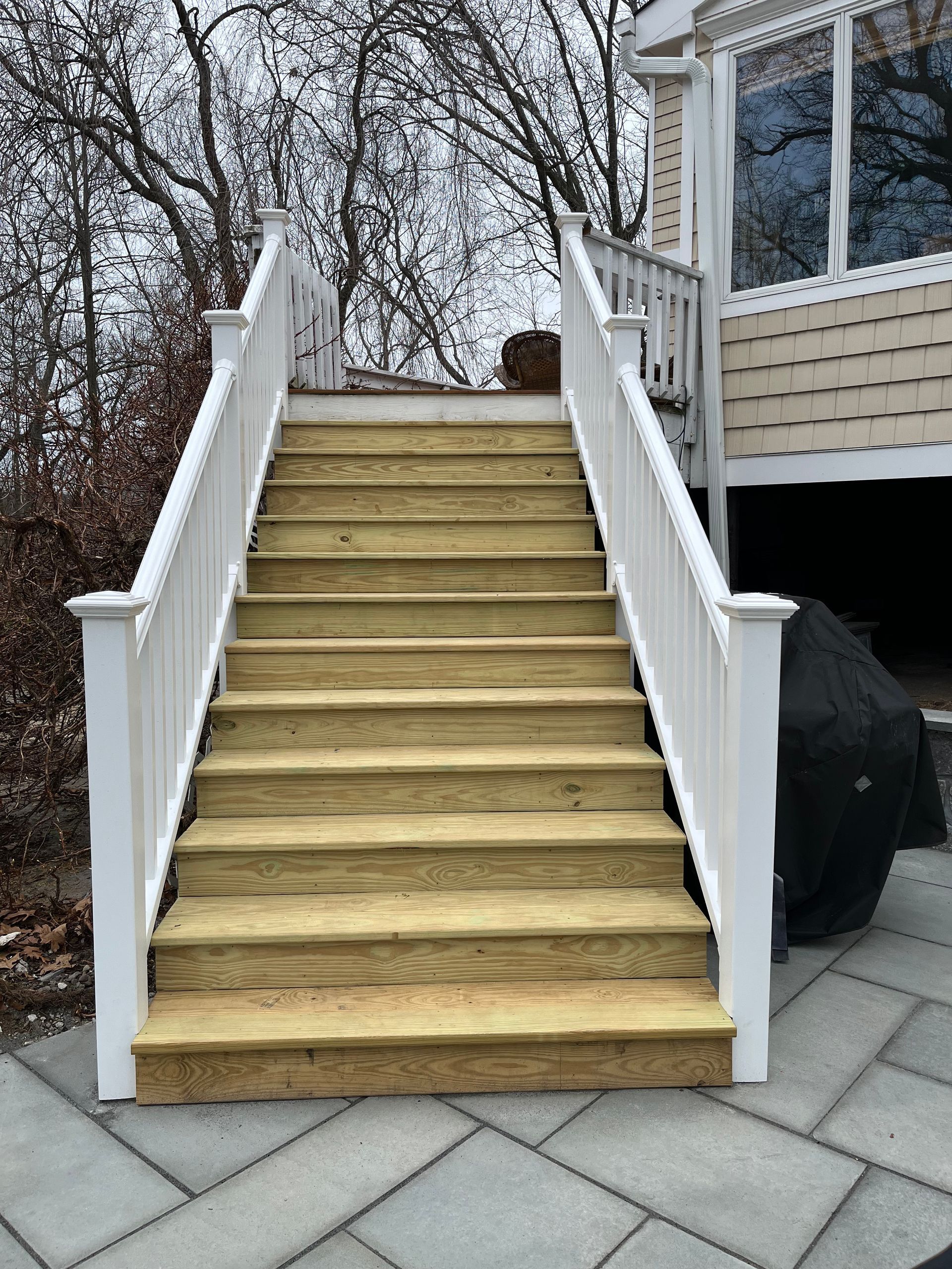Wooden outdoor staircase with white railings leading up to a deck.