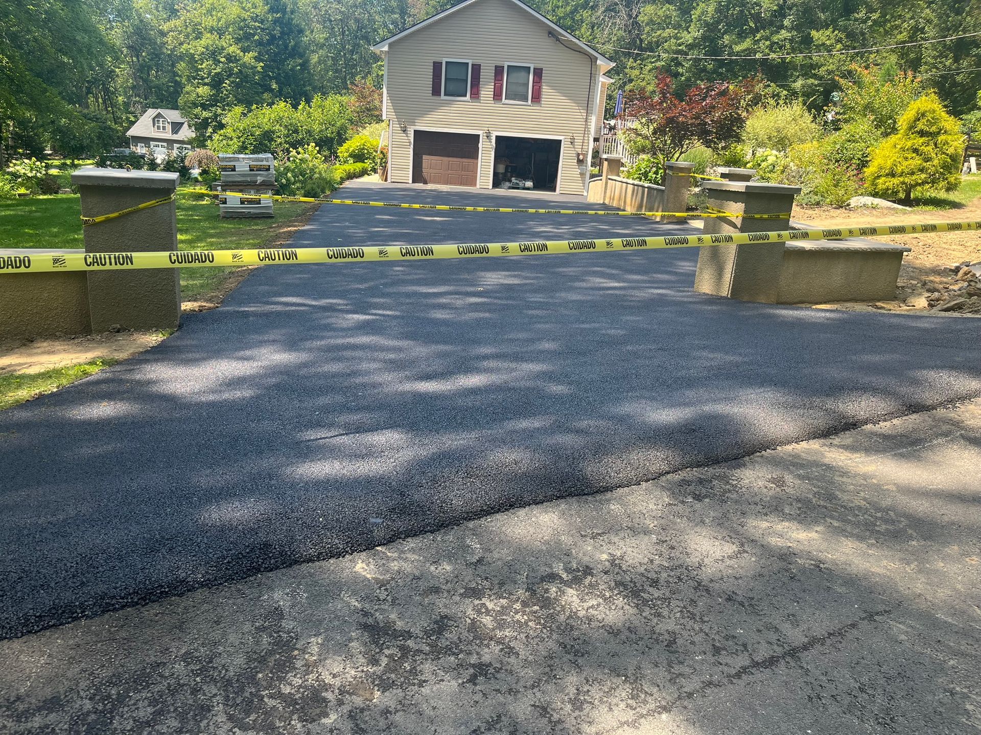 Beige stone patio with long shadow from wooden railing, bordering a retaining wall and greenery.