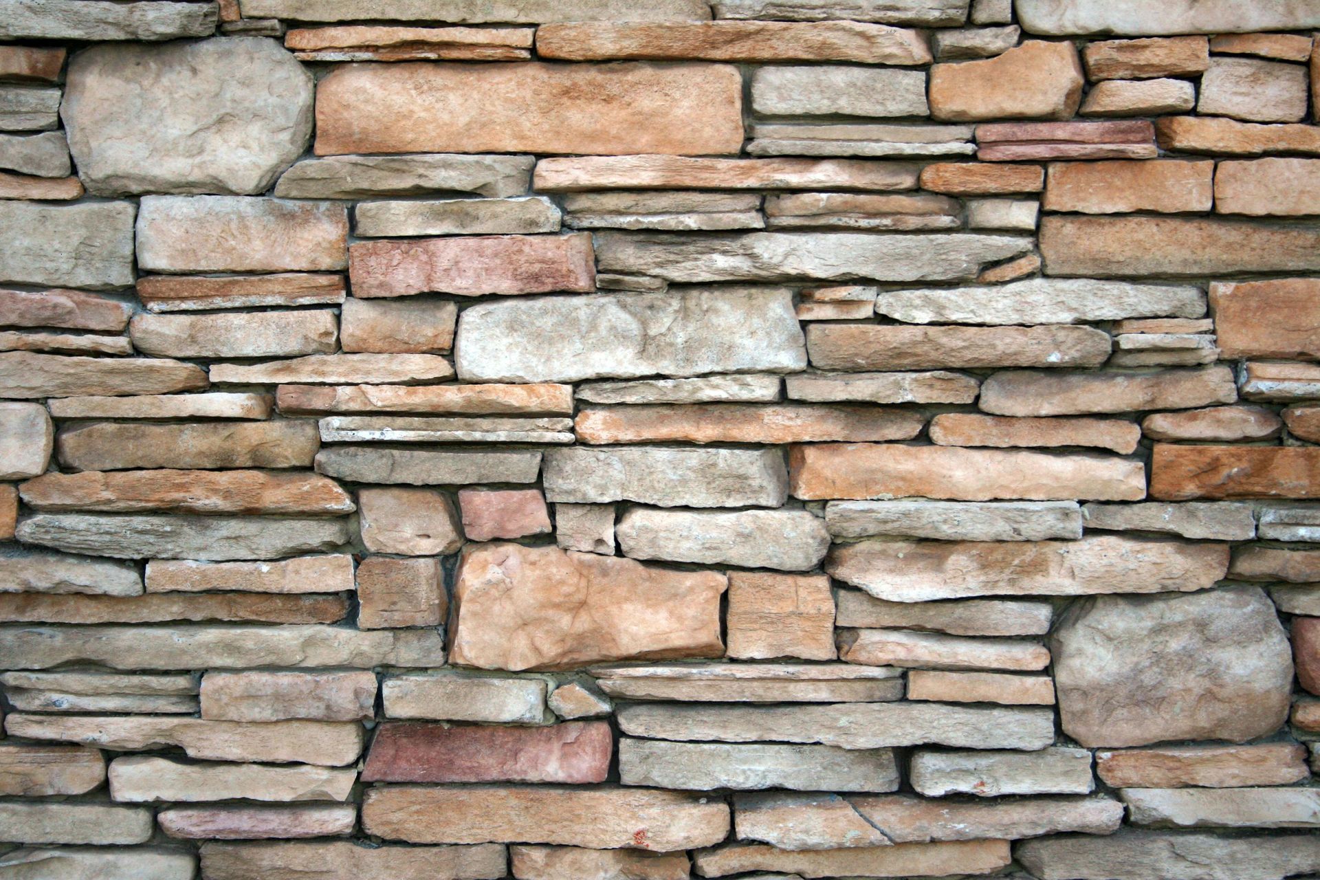 Stone wall with mixed browns, grays, and tan stones, mortared together.