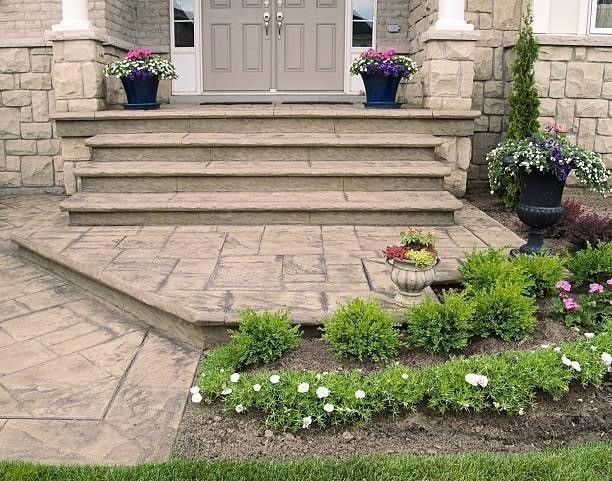 Wooden staircase with white railings leading up to a house on a gray stone patio.