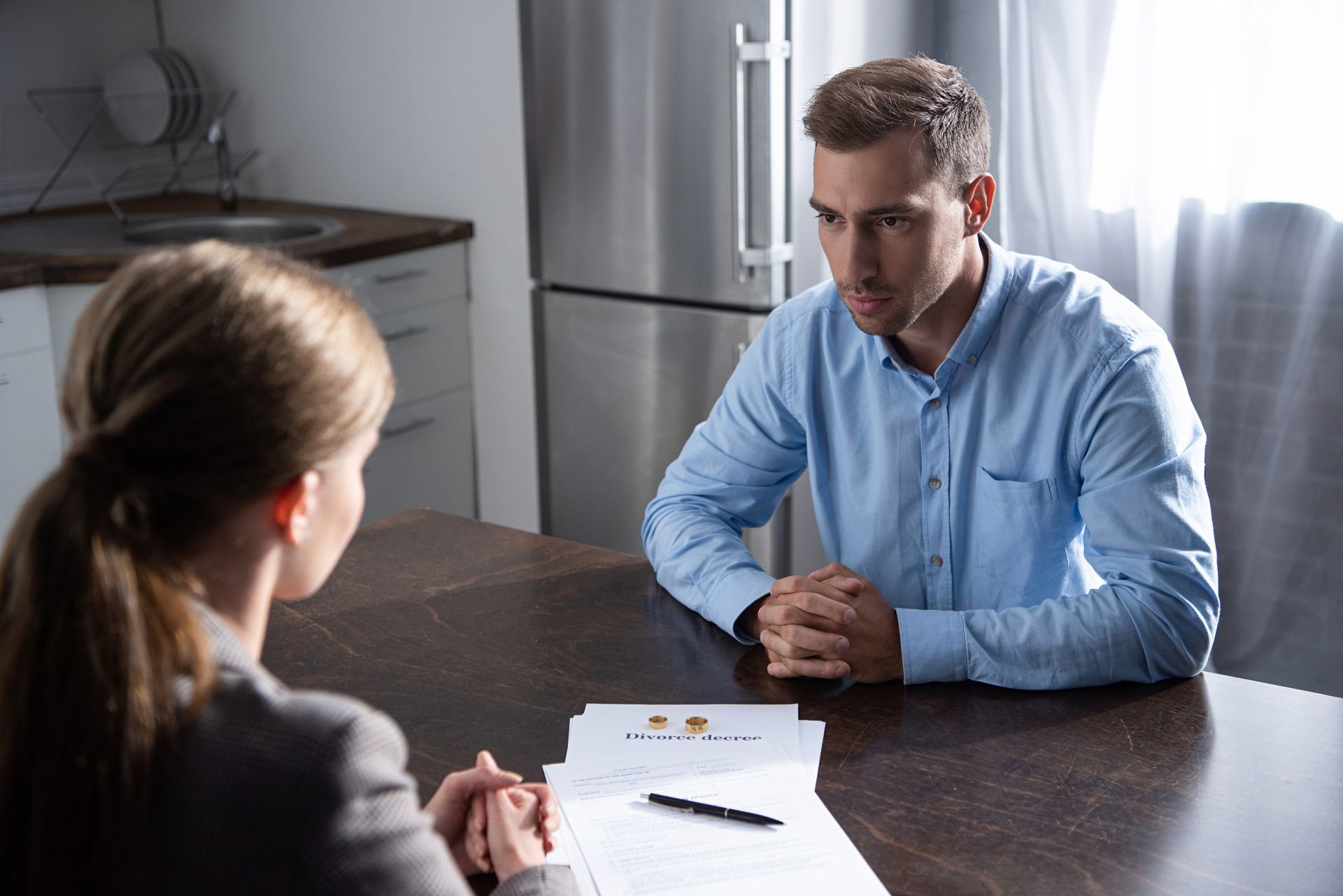 Man at table with woman, discussing paperwork in a kitchen.