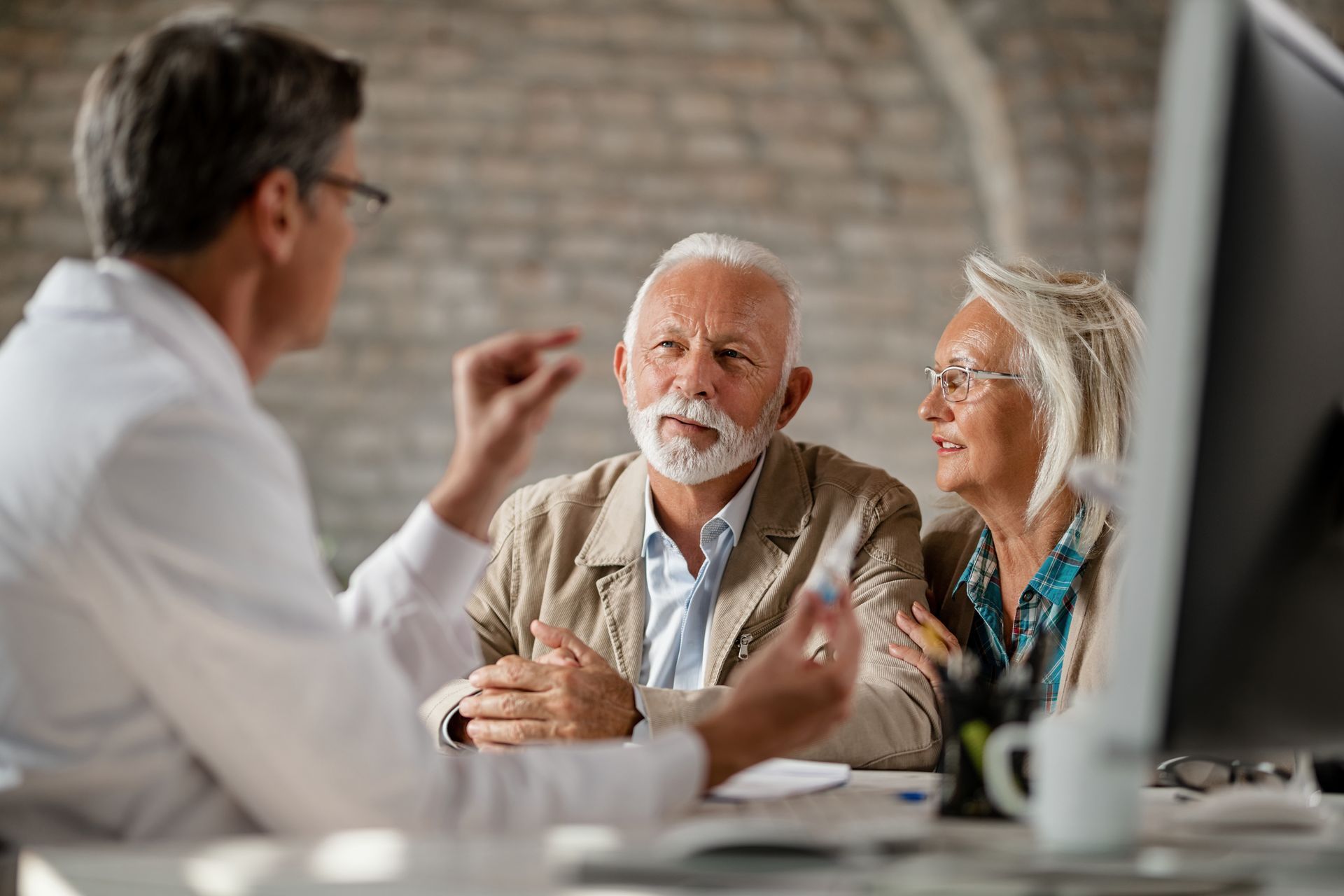 Doctor talking with an older couple at a desk in a medical office.