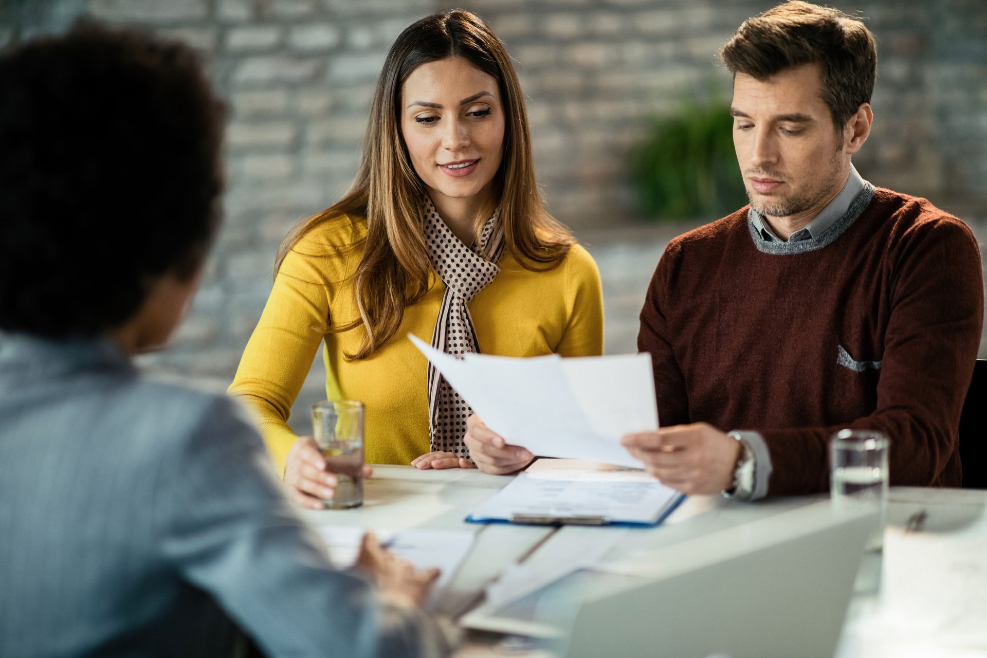 Three people reviewing paperwork at a table; a woman and man looking at papers, another person talking.