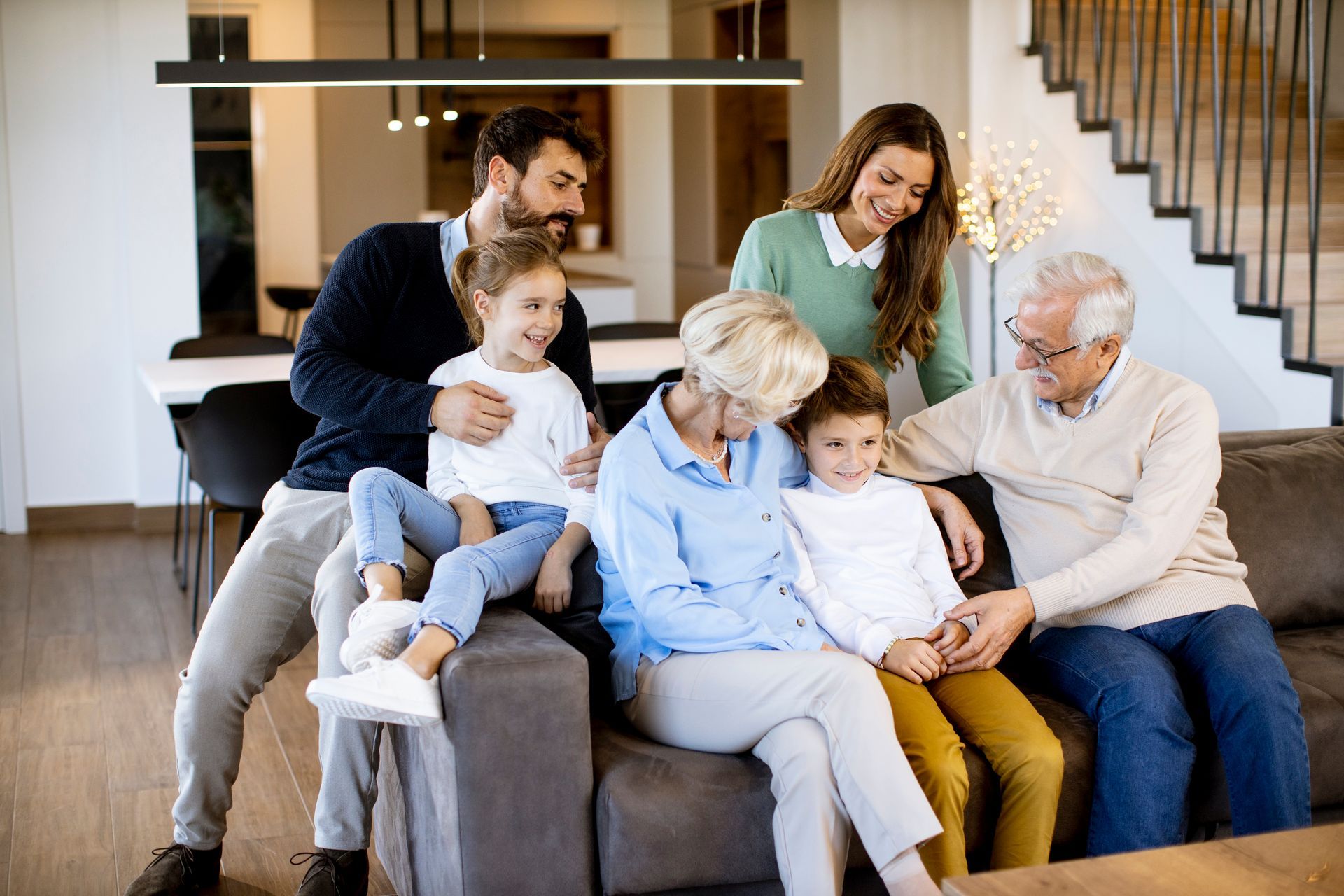 Family of seven smiles together on a couch in a modern living room.