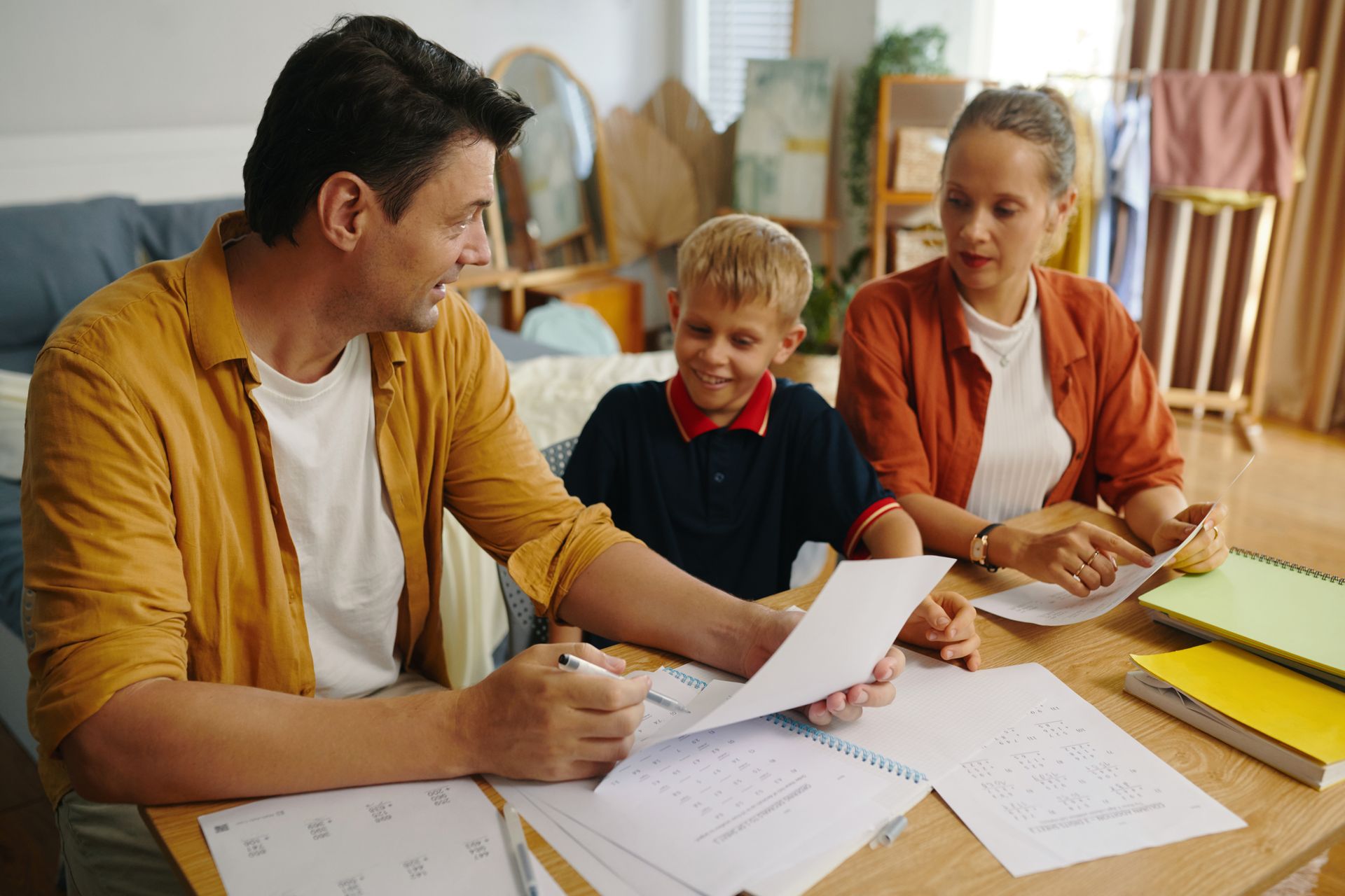 Family sitting at a table reviewing papers; smiling child between parents in a home setting.