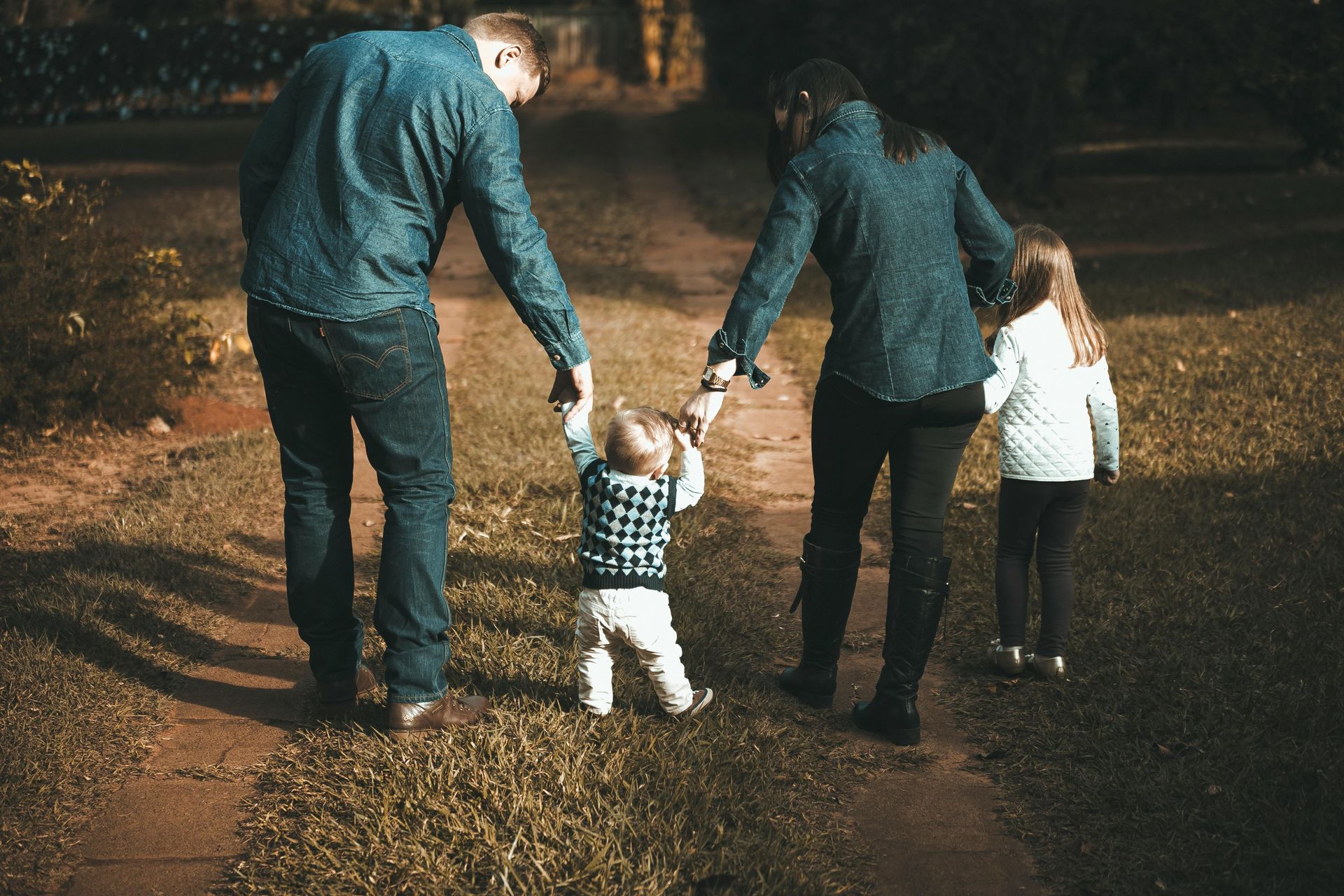 Family holding hands, walking down a path; child in the middle, others wearing blue and white.